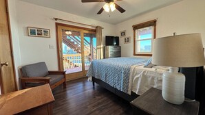 A bedroom with a bed, a chair, a desk, a lamp, a TV, and a window with a view of a building. -     7BR Coastal Escape ,Ocean and Sound Views, Pool, Hot Tub & Pet Friendly (Rodanthe)