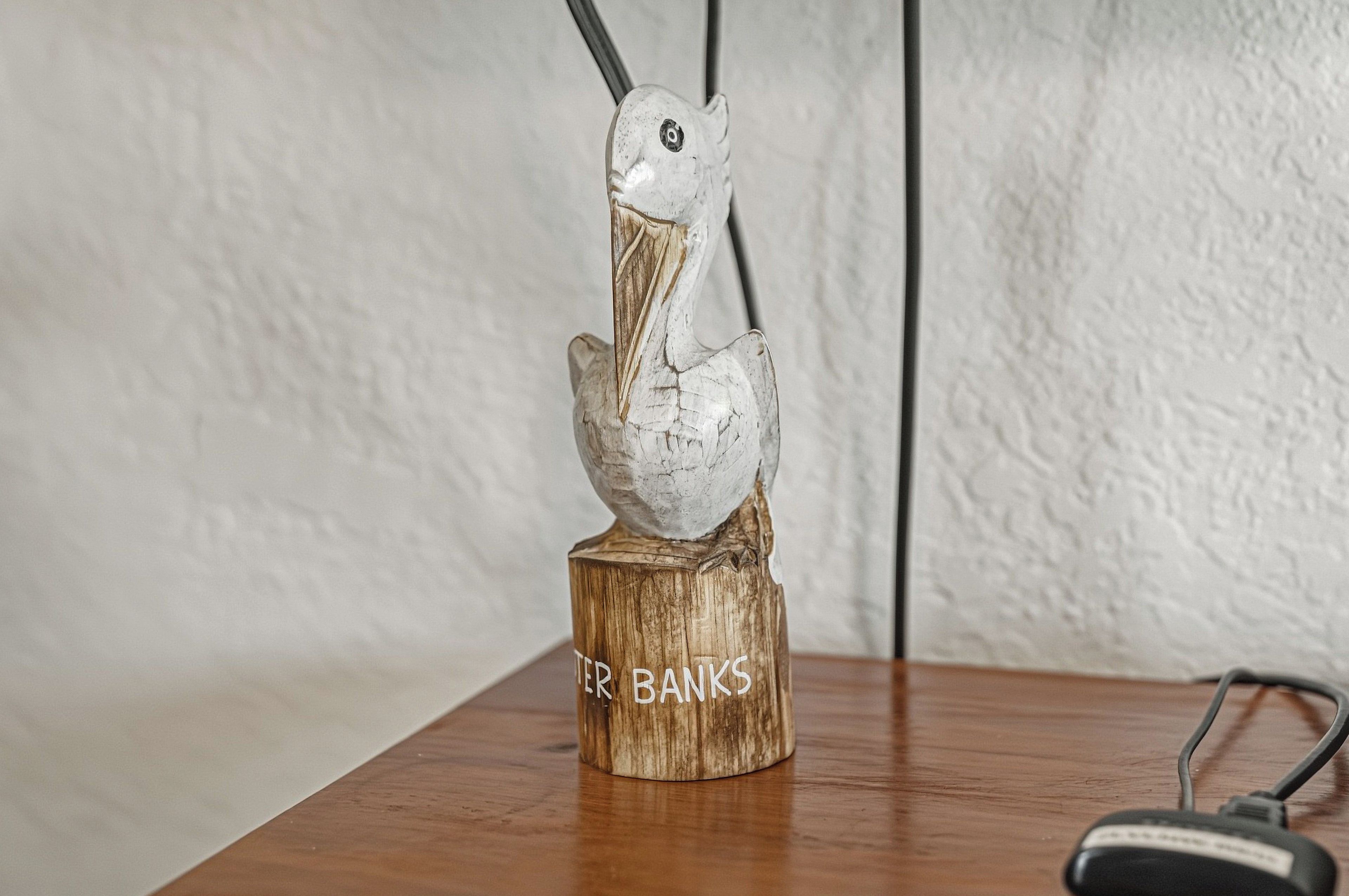 A wooden sculpture of a bird on a table with a cable and a pair of headphones beside it.