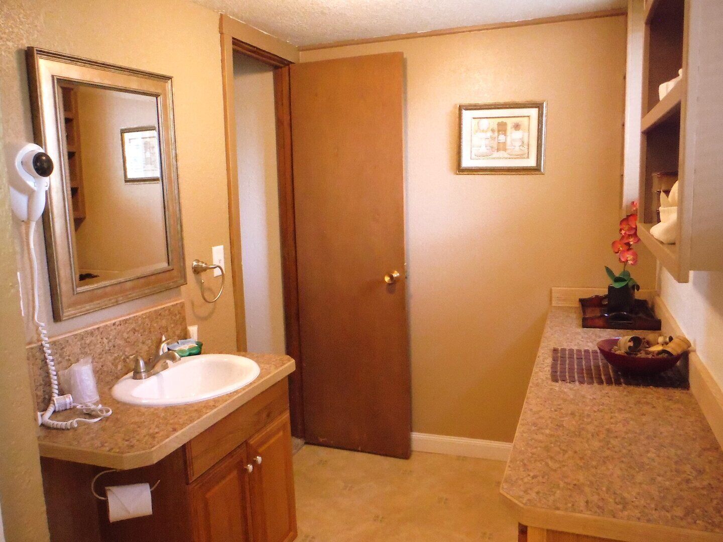 Une salle de bain équipée d’un lavabo, d’un miroir, d’une porte et d’une petite étagère sur laquelle sont disposés des objets décoratifs.