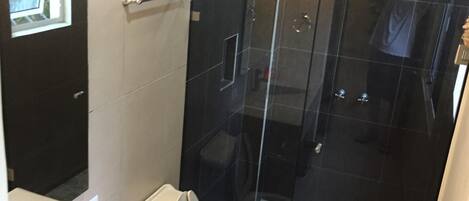 A modern bathroom with a glass-enclosed shower, a toilet, and a sink.