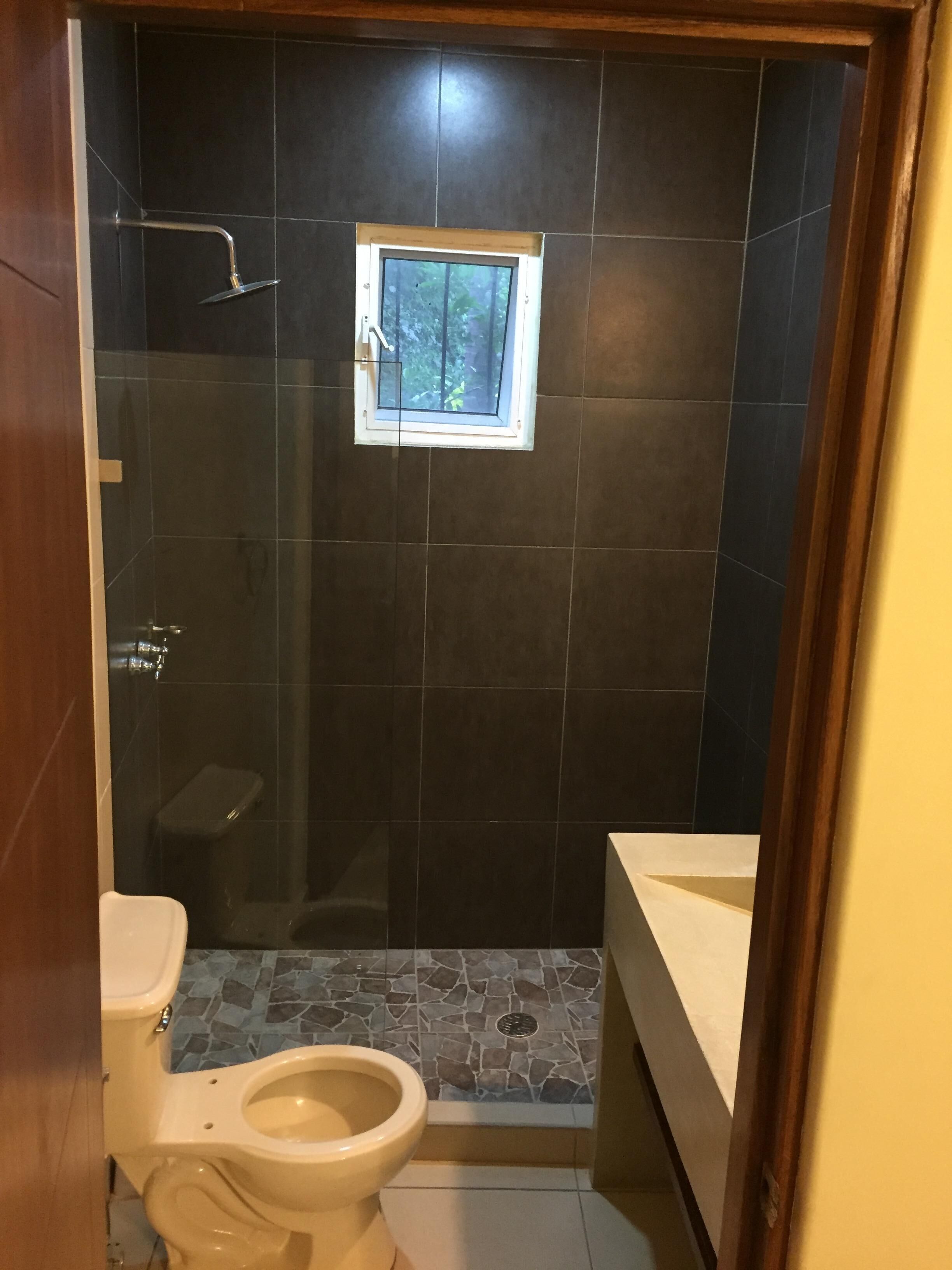 Et badeværelse med bruser, toilet og et vindue.