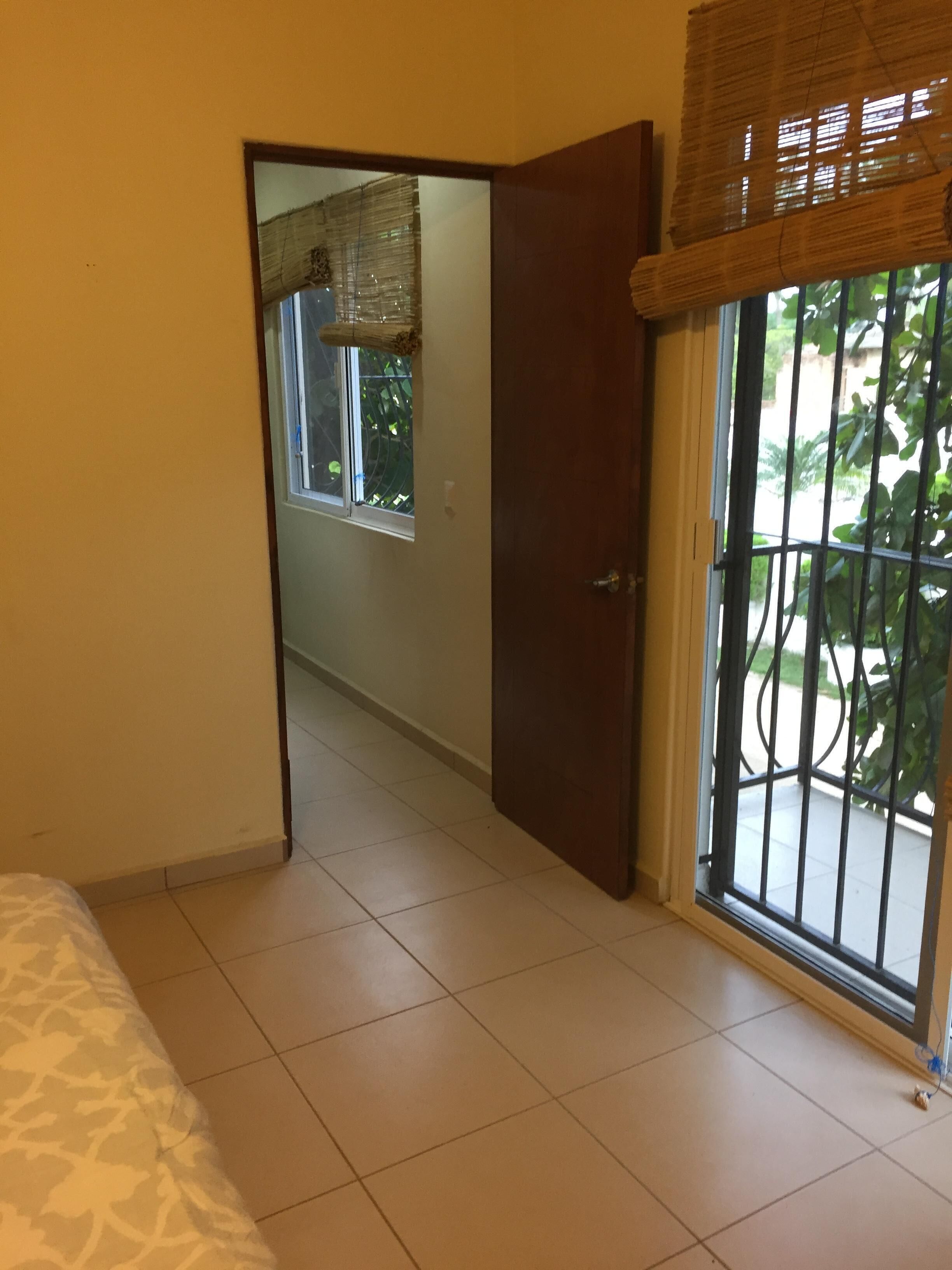Une chambre d’hôtel avec un lit, une porte donnant sur un balcon avec vue sur la verdure, et une fenêtre donnant sur l’extérieur.