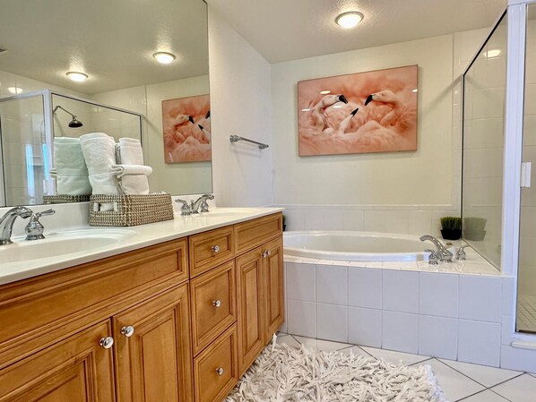 Un baño moderno con un tocador de madera, dos lavamanos, un espejo grande y una bañera.
