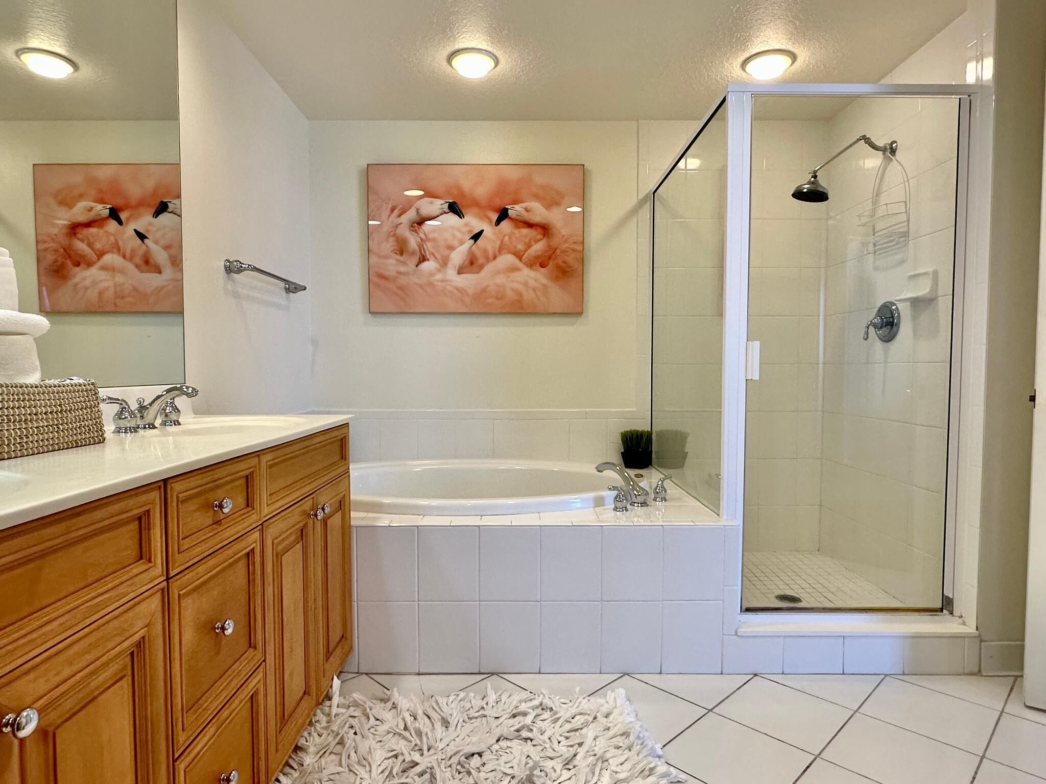Ein modernes Badezimmer mit einem Holzwaschtisch, einer großen Badewanne, einer gläsernen Dusche und zwei an der Wand befestigten Kunstwerken.