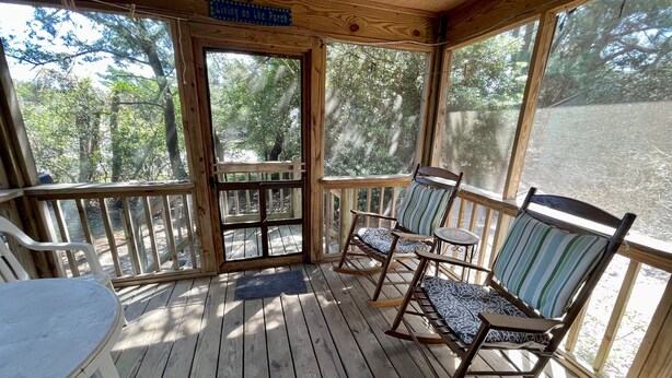 A wooden porch with rocking chairs and a table, overlooking a forested area. - Off The Beaten Path:  Surrounded by trees and nicely secluded. (Ocracoke)