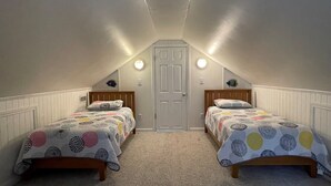 A bedroom with two single beds, a door, and a sloped ceiling. - Off The Beaten Path:  Surrounded by trees and nicely secluded. (Ocracoke)