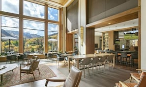 A spacious indoor area with large windows offering a mountain view, wooden furniture, and a bar area.
