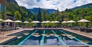 A pool area with lounge chairs and umbrellas, surrounded by mountains and greenery.