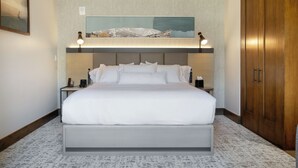 Quarto de hotel moderno com uma cama grande, duas mesas de cabeceira, um criado-mudo, um guarda-roupa de madeira e um quadro com uma paisagem acima da cama.