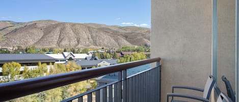 Un balcon donnant sur un paysage montagneux, un bâtiment doté d’un toit en pente et une chaise.