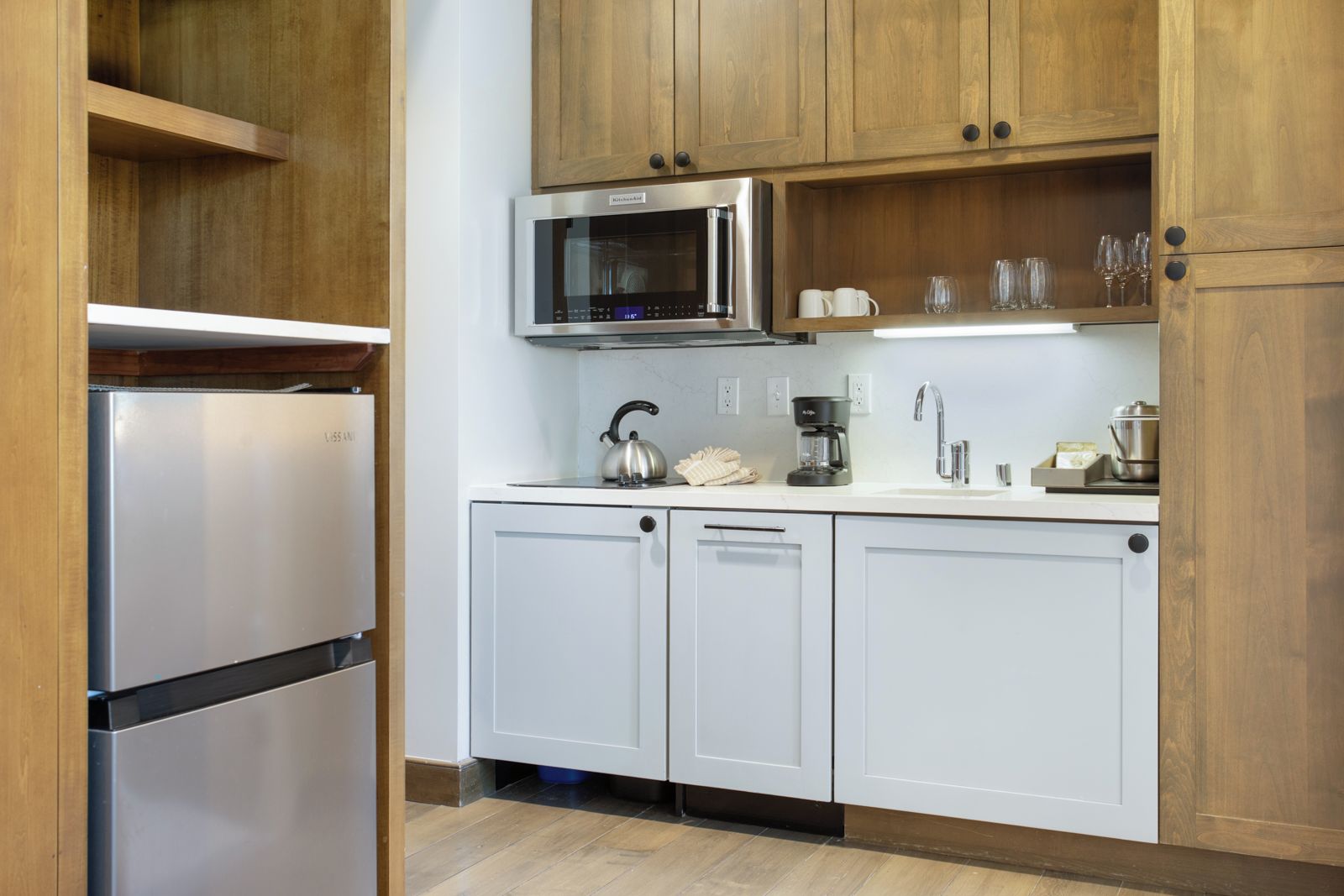 A kitchen with white cabinets, a stainless steel refrigerator, a microwave, and a coffee maker.