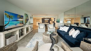 A living room with a TV, a sofa, a coffee table, and a kitchen in the background.