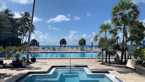 A swimming pool with a view of the ocean, surrounded by palm trees and lounge chairs.