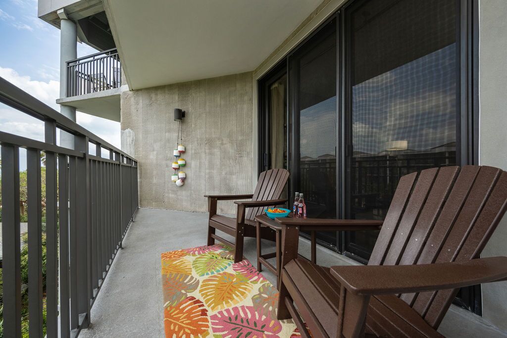 A balcony with two wooden chairs, a small table, and a colorful rug.