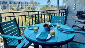 A balcony with a table set for two, featuring a bowl of fruit, two glasses of juice, and a napkin.