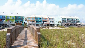 Une promenade en bois mène à des bâtiments colorés situés en bord de mer, dotés de balcons et d’espaces de repos en plein air.