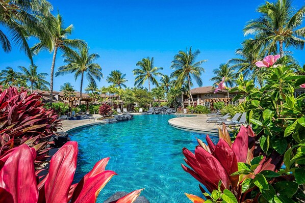 A resort pool with palm trees and red foliage.