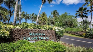 Un panneau indiquant l’emplacement de Waikoloa Colony Villas, avec une route menant à l’établissement, le tout entouré d’une végétation luxuriante et de palmiers.