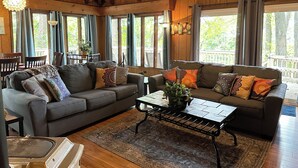 A cozy living room with two sofas, a coffee table, and a ceiling fan. Large windows with curtains provide natural light and views of the outdoors. - Bedrooms 4, Bathrooms 2, Sleeps 10 (Front Royal)