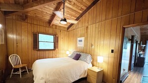 A bedroom with a wooden ceiling, a bed with white bedding, a nightstand with a lamp, a window with shutters, and a chair. - Bedrooms 4, Bathrooms 2, Sleeps 10 (Front Royal)