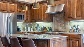 Una cocina con armarios de madera, electrodomésticos de acero inoxidable, encimera de granito e iluminación colgante.