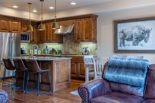 A modern kitchen with wooden cabinets, stainless steel appliances, and a central island with bar stools. - Skiview Townhome 1B - Centralized Ketchum Vacation Pad (Ketchum)