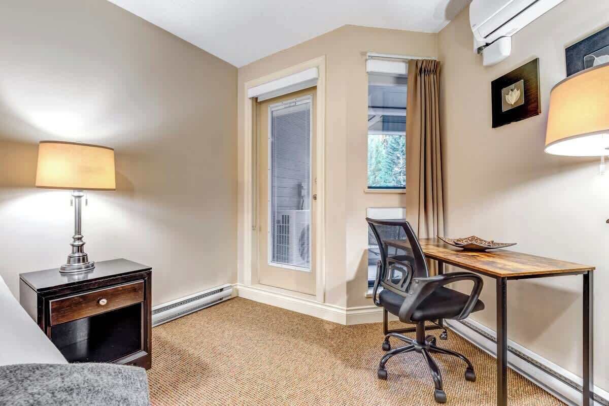 Une chambre d’h ôtel équipée d’un bureau, d’une chaise, d’une lampe et d’une fenêtre avec des rideaux.