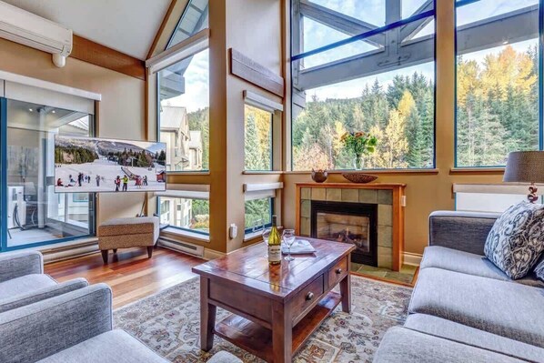 A spacious living room with a fireplace, large windows, and a view of a snowy landscape. - Greystone Lodge 408 Ski-in/Out by Acer Vacations (Whistler)