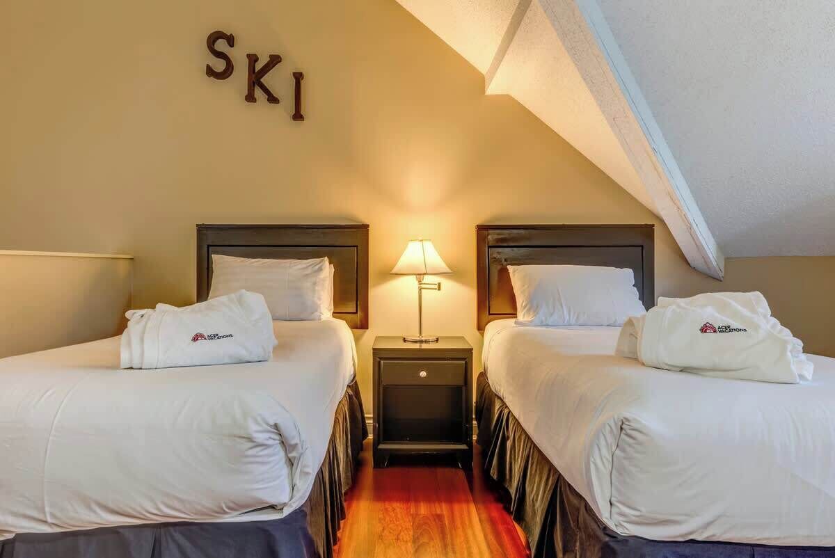A hotel room with two beds, a nightstand with a lamp, and a wall sign that reads 'SKI'.