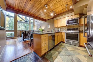 A modern kitchen with wooden cabinets, stainless steel appliances, and large windows.