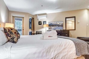 A hotel room with a bed, two bedside lamps, a dresser, a television, and a painting on the wall. - Greystone Lodge 408 Ski-in/Out by Acer Vacations (Whistler)