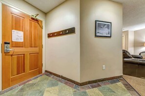 A hallway with a wooden door, a coat rack, a framed picture, and a leather sofa in the background.