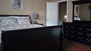 A bedroom with a bed, a dresser, a nightstand, a lamp, and a door. - A BEAUTIFUL 3 BEDROOM BUNGALOW WITH ALL MODERN AMENITIES  CLOSE TO A PARK!! (Dayton)