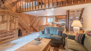 L’intérieur d’un chalet accueillant, avec un plafond en bois, un canapé, une table basse et, au fond, un coin cuisine.