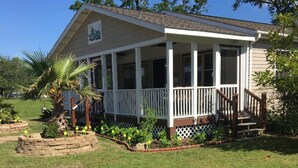 Einbungalow mit Veranda, umgeben von einem Garten mit verschiedenen Pflanzen und einer Palme.