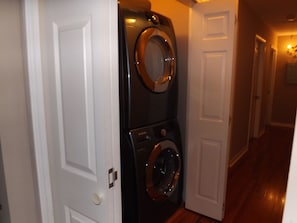 Une buanderie équipée de machines à laver et de sèche-linge superposés, avec un plancher en bois et des portes blanches.
