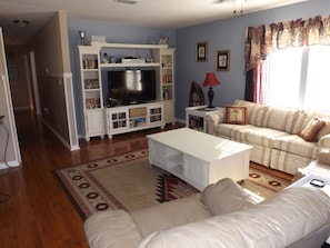 Un salon avec un meuble de rangement blanc pour l’équipement audiovisuel, un téléviseur à écran plat, un canapé et une table basse.