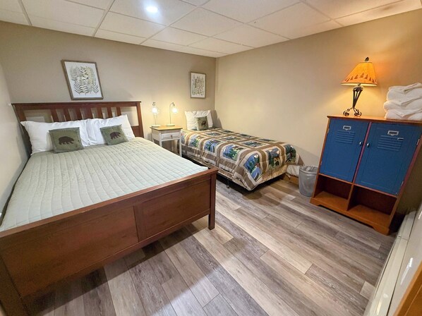 A bedroom with a large bed, a smaller bed, a nightstand with lamps, a wardrobe, and two framed pictures on the wall.
