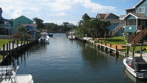 A canal with boats docked on the left and a dock on the right. - Blind Mullet:  Family friendly, den, decks, deep water private dock. (Ocracoke)