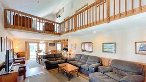 A spacious living room with a high ceiling, wooden staircase, and a dining area. - Blind Mullet:  Family friendly, den, decks, deep water private dock. (Ocracoke)