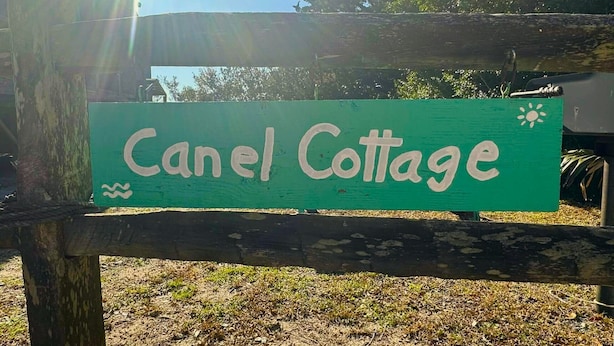 A wooden sign with the text "Canel Cottage" on a green background. - Canel Cottage:  Tucked in the trees, nearby kayak launch area. (Ocracoke)
