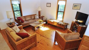 A cozy living room with a wooden floor, a brown sofa, a wooden coffee table, and a television on a wooden stand. - Canel Cottage:  Tucked in the trees, nearby kayak launch area. (Ocracoke)