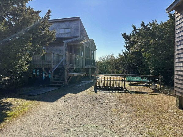 A two-story wooden building with a porch and steps leading to a deck. - Canel Cottage: Tucked in the trees, nearby kayak launch area. (Ocracoke)