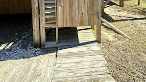 A wooden playhouse with a ladder leading up to a door, situated on a wooden deck in front of a house. - Canel Cottage:  Tucked in the trees, nearby kayak launch area. (Ocracoke)