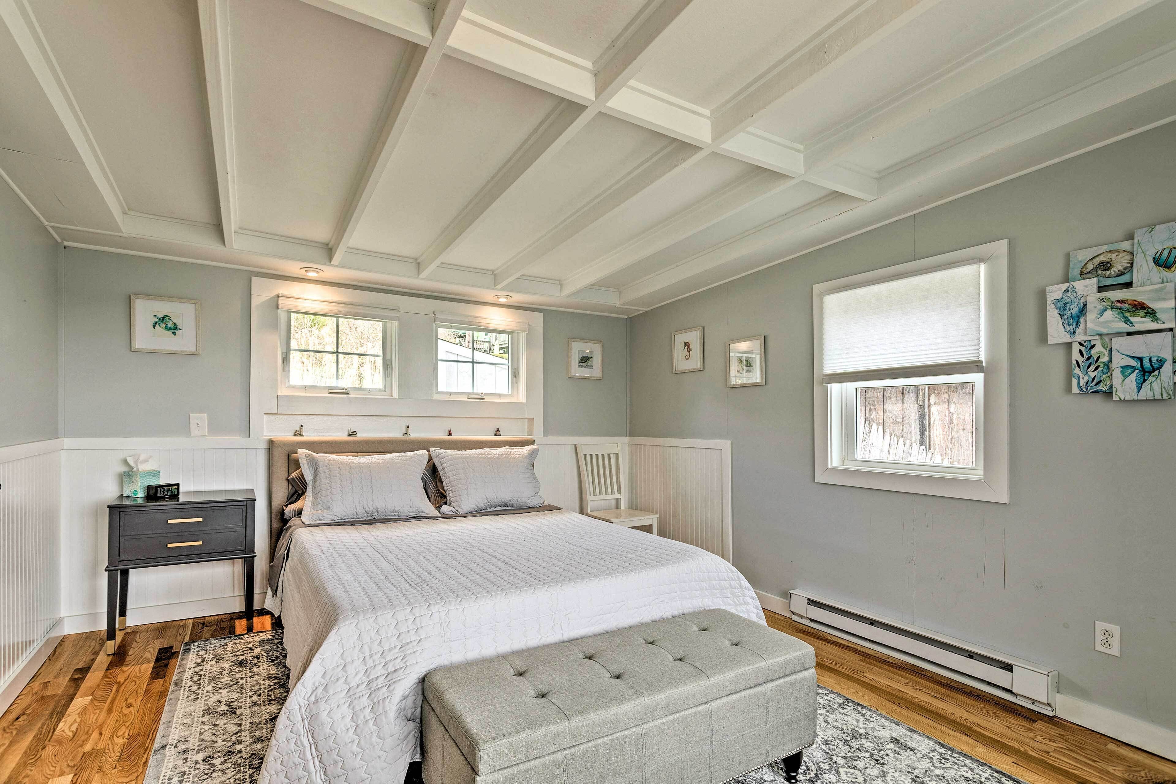 A bedroom with a large bed, a nightstand, a bench, and a window with blinds.