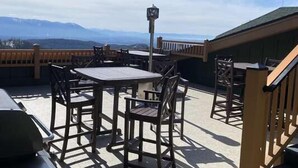 An outdoor patio with wooden tables and chairs, a clock, and a view of mountains. - Ski-In/Ski-Out Condo with Valley Views (Whitefish)