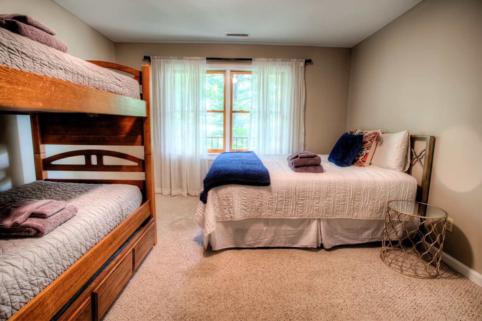 A bedroom with two bunk beds, a single bed, a small round table, and a window with curtains.
