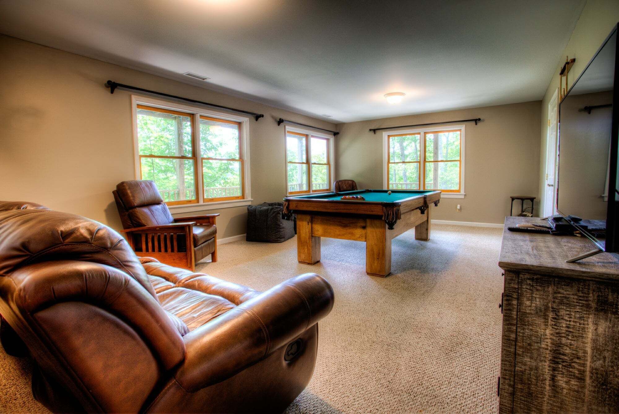 Una habitación con mesa de billar, sillón de cuero y ventanas amplias.