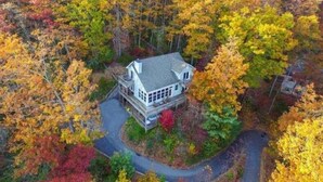 A house surrounded by autumn foliage, with a driveway leading to the entrance.