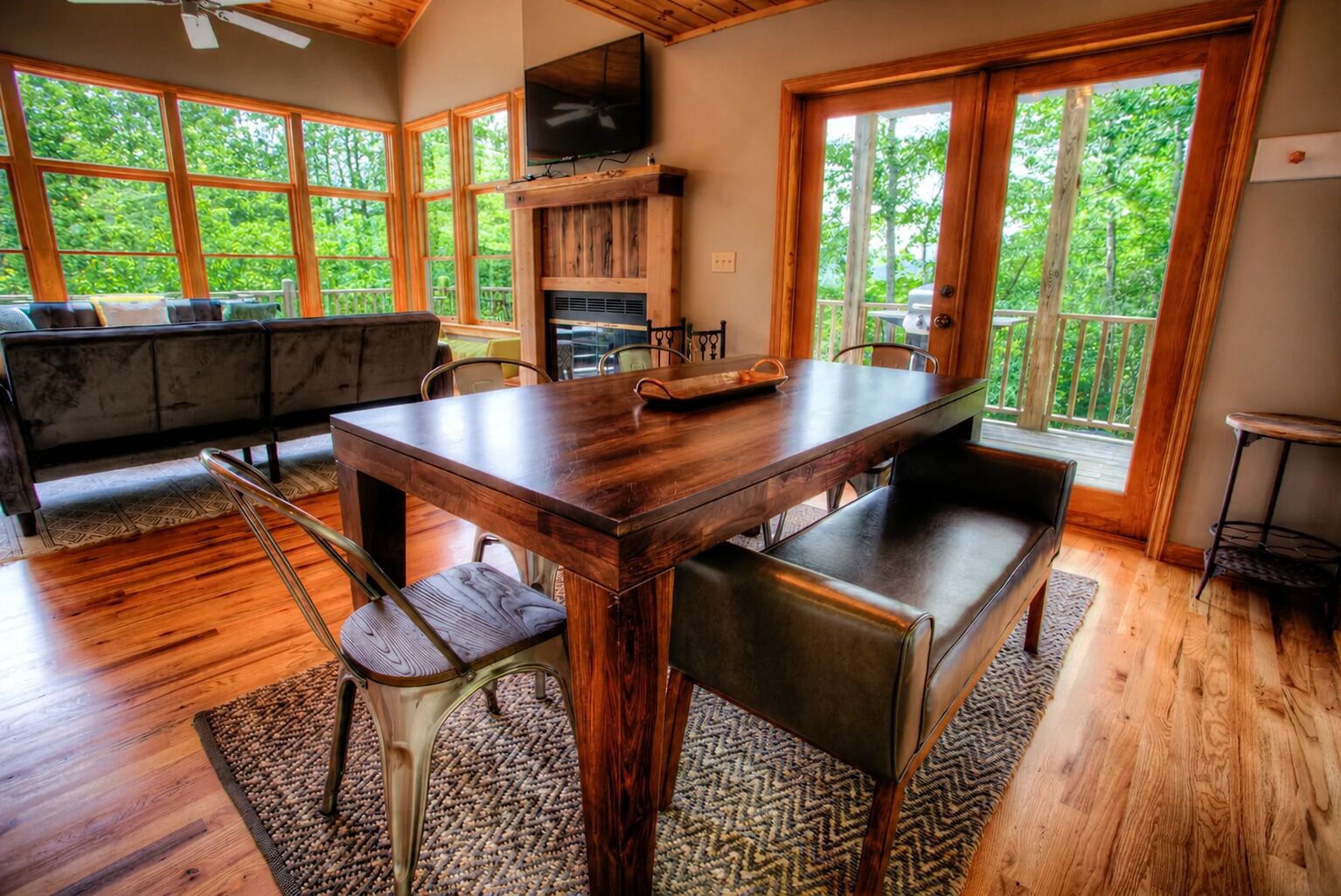 Una mesa de madera con sillas, un banco, un televisor y una chimenea.